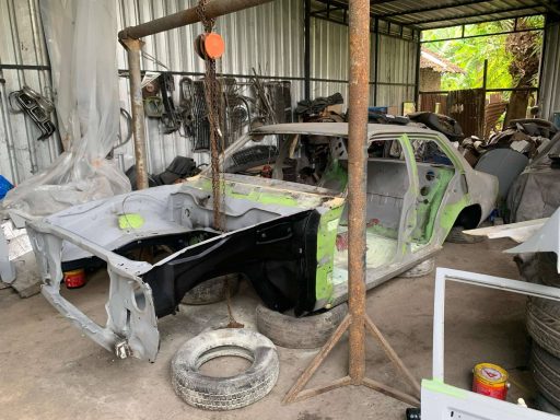 Partially disassembled car chassis in a cluttered workshop.